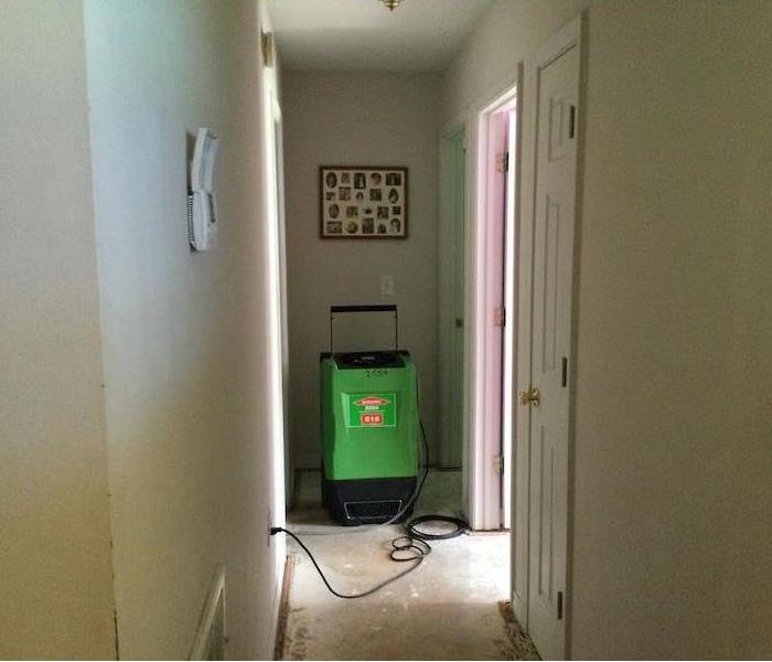 Hallway with subfloor exposed and SERVPRO dehumidifier 