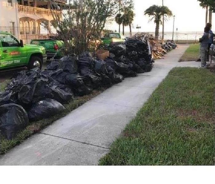 long line of black garbage bags piled on street after storm