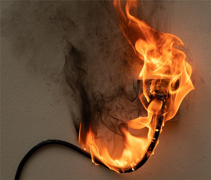 an outlet on fire with the wire plugged into it also on fire